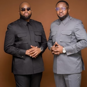 May include: Two people wearing matching tailored shirts and pants. One outfit is black, the other is gray. Both outfits have a collared neckline and four front pockets. Each person wears a wristwatch and glasses.