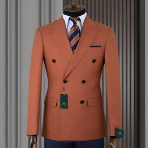 Pode incluir: Casaco de fato cor de ferrugem de abotoamento duplo com bot&otilde;es pretos, gravata listrada azul marinho e laranja e camisa branca. O fato &eacute; exibido em um manequim com cal&ccedil;as azul marinho.