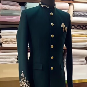 Puede incluir: Chaqueta verde oscuro con cuello mandar&iacute;n y botones dorados. La chaqueta presenta bordados dorados en los pu&ntilde;os y un broche decorativo dorado en el pecho. La chaqueta se exhibe en un maniqu&iacute;.
