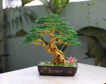 Puede incluir: Una escultura decorativa de árbol bonsái con un tronco y ramas de alambre trenzado de color dorado, adornados con pequeñas cuentas verdes que representan hojas. El árbol está colocado en una maceta rectangular de cerámica marrón.