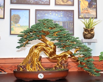 May include: A handcrafted wire bonsai tree sculpture featuring a thick, twisted metallic gold trunk and branches adorned with numerous small, vibrant green wire leaves. The sculpture is anchored in a shallow, oval-shaped brown ceramic pot.