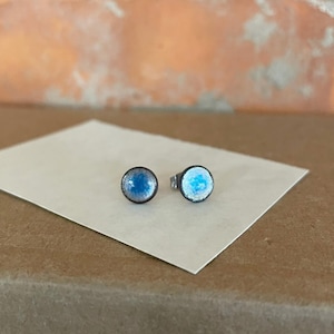 May include: A pair of small, round stud earrings with a silver base and a blue and white enamel design.