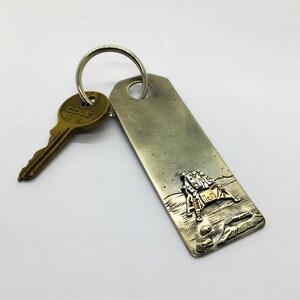 May include: Silver key chain with a gold-toned lunar lander design and a brass key with the text "COLE" and "1118".