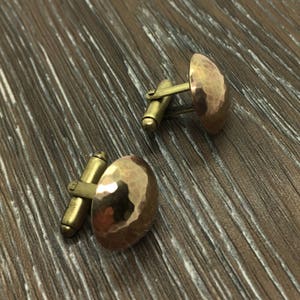 May include: A pair of gold-toned cufflinks with a hammered finish. The cufflinks are round and have a slightly domed shape.
