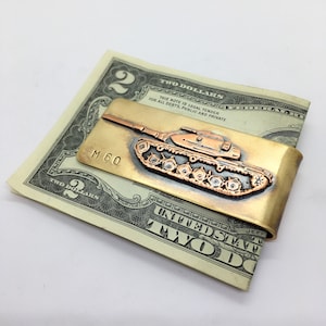 May include: A brass money clip with a copper-colored tank embossed on it. The tank is labeled "M 60".