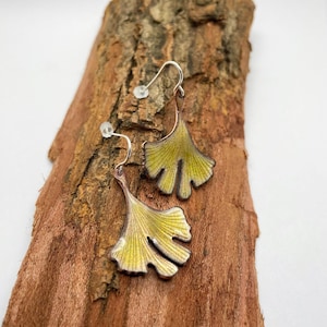 May include: A pair of silver dangle earrings with yellow ginkgo leaf charms. The leaves are detailed with veins and have a slightly textured surface.