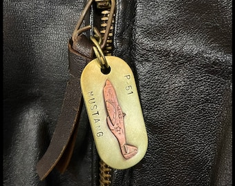 May include: A brass key chain with a P-51 Mustang airplane design. The keychain is attached to a brown leather jacket zipper.