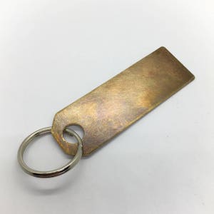 Puede incluir: Un llavero de lat&oacute;n con un anillo de llave de plata. La etiqueta tiene un acabado cepillado y una forma ligeramente rectangular.