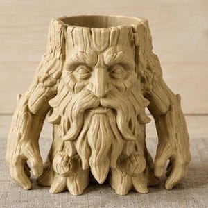 Puede incluir: Un recipiente cilíndrico de color bronceado claro con forma de tocón de árbol y un rostro esculpido con barba, bigote y cejas prominentes. La textura exterior imita la corteza de un árbol y el objeto incluye dos extensiones como brazos.