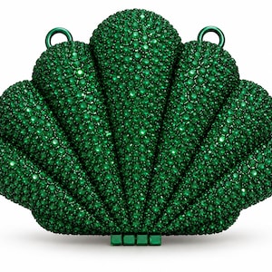May include: A shell-shaped clutch bag covered in small, sparkling emerald green crystals. The bag features a scalloped design with a textured surface, two circular metal rings at the top for attachment, and a small rectangular clasp at the base.