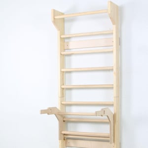 May include: A wooden climbing wall with multiple horizontal bars and a pull-up bar attachment. The wall is made of light-colored wood and is mounted against a white wall. The design is for indoor use.