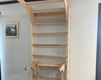 Könnte beinhalten: Eine wandmontierte Sprossenwand aus hellem Holz mit einer Reihe horizontaler Sprossen, einem oberen Klimmzugbereich, der nach außen ragt, und einem abnehmbaren, kleineren Leiteraufsatz, der in der Mitte des Hauptrahmens angebracht ist.