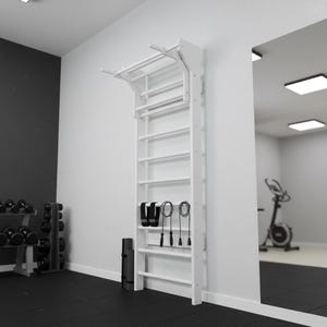 Puede incluir: Una espaldera de gimnasia de madera blanca montada en la pared con una barra de dominadas superior. La estructura tipo escalera incluye varios pelda&ntilde;os horizontales, con una cuerda de saltar y dos correas de tobillo negras colgadas de un pelda&ntilde;o.
