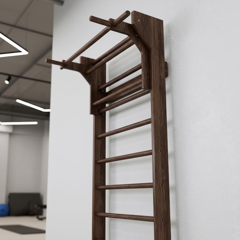 Puede incluir: Una unidad de espaldera de madera de color marr&oacute;n oscuro montada en la pared, que cuenta con una serie de pelda&ntilde;os horizontales y una extensi&oacute;n de barra de dominadas integrada en la parte superior. La estructura consta de paneles laterales.