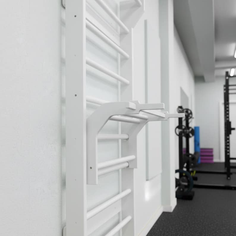 Puede incluir: Una espaldera blanca montada en la pared que presenta una serie de pelda&ntilde;os horizontales y un accesorio de barra de dominadas desmontable que se extiende hacia afuera. La estructura es de material blanco s&oacute;lido y est&aacute; fijada a la pared.
