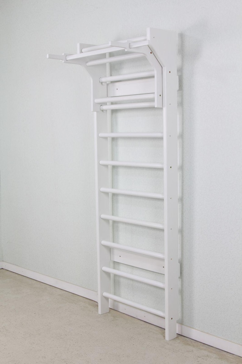 Puede incluir: Una espaldera de madera blanca montada en la pared con un dise&ntilde;o de escalera vertical, m&uacute;ltiples pelda&ntilde;os horizontales y una extensi&oacute;n de barra de dominadas integrada en la parte superior. Estructura de madera maciza con acabado blanco.