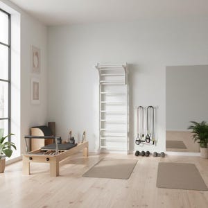 Puede incluir: Una espaldera de madera blanca montada en la pared con pelda&ntilde;os horizontales y una barra de dominadas superior, situada en una habitaci&oacute;n junto a una m&aacute;quina de Pilates de madera clara, dos bandas de resistencia y dos mancuernas peque&ntilde;as.