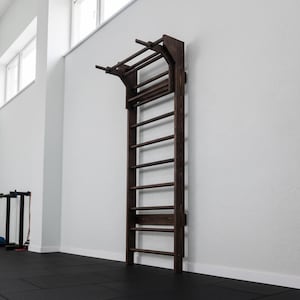 Puede incluir: Una espaldera de madera de color marr&oacute;n oscuro montada en la pared, que cuenta con una serie de pelda&ntilde;os horizontales y una extensi&oacute;n de barra de dominadas integrada en la parte superior. El equipo de ejercicio tiene soportes laterales.