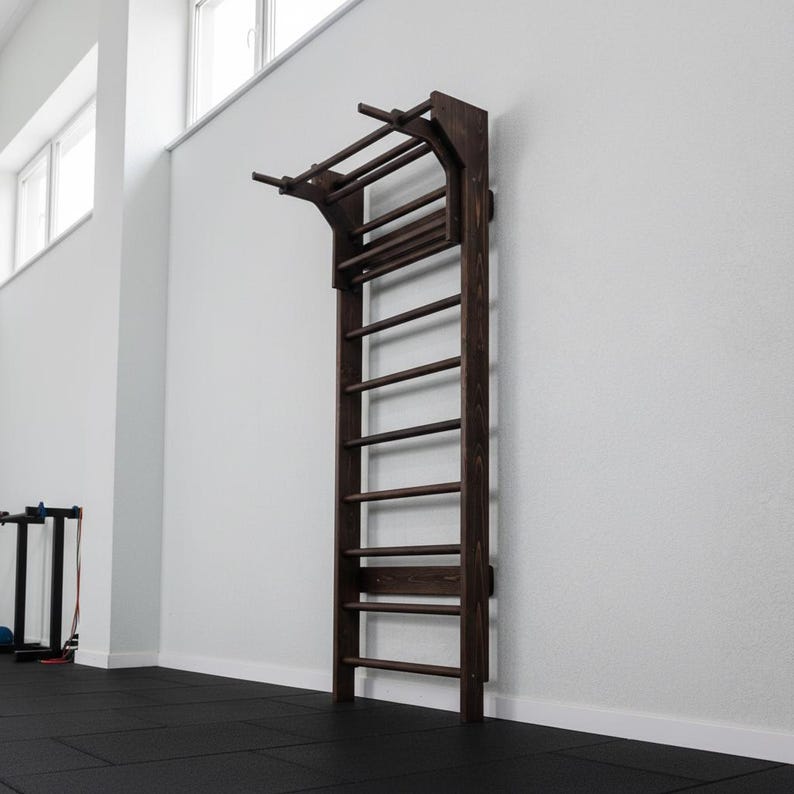 Puede incluir: Una espaldera de madera de color marr&oacute;n oscuro montada en la pared, que cuenta con una serie de pelda&ntilde;os horizontales y una extensi&oacute;n de barra de dominadas integrada en la parte superior. El equipo de ejercicio tiene soportes laterales.