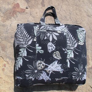 May include: A black tote bag with a white and green leaf pattern. The bag has a large pocket on the front.