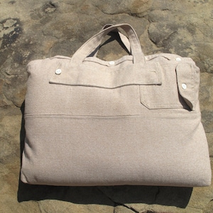 May include: A beige linen tote bag with two button closures and a pocket on the front.