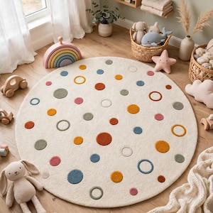 May include: A round, cream-colored area rug featuring a scattered pattern of multi-colored circles in shades of blue, orange, green, and pink. Some circles are solid, while others are outlined, creating a textured, playful design on the floor.