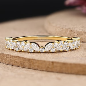May include: A gold band ring featuring a series of marquise and round cut clear stones arranged in a leaf-like pattern along the top half of the band. The ring has a polished yellow gold finish and includes the text Veloura Diamond in the corner.