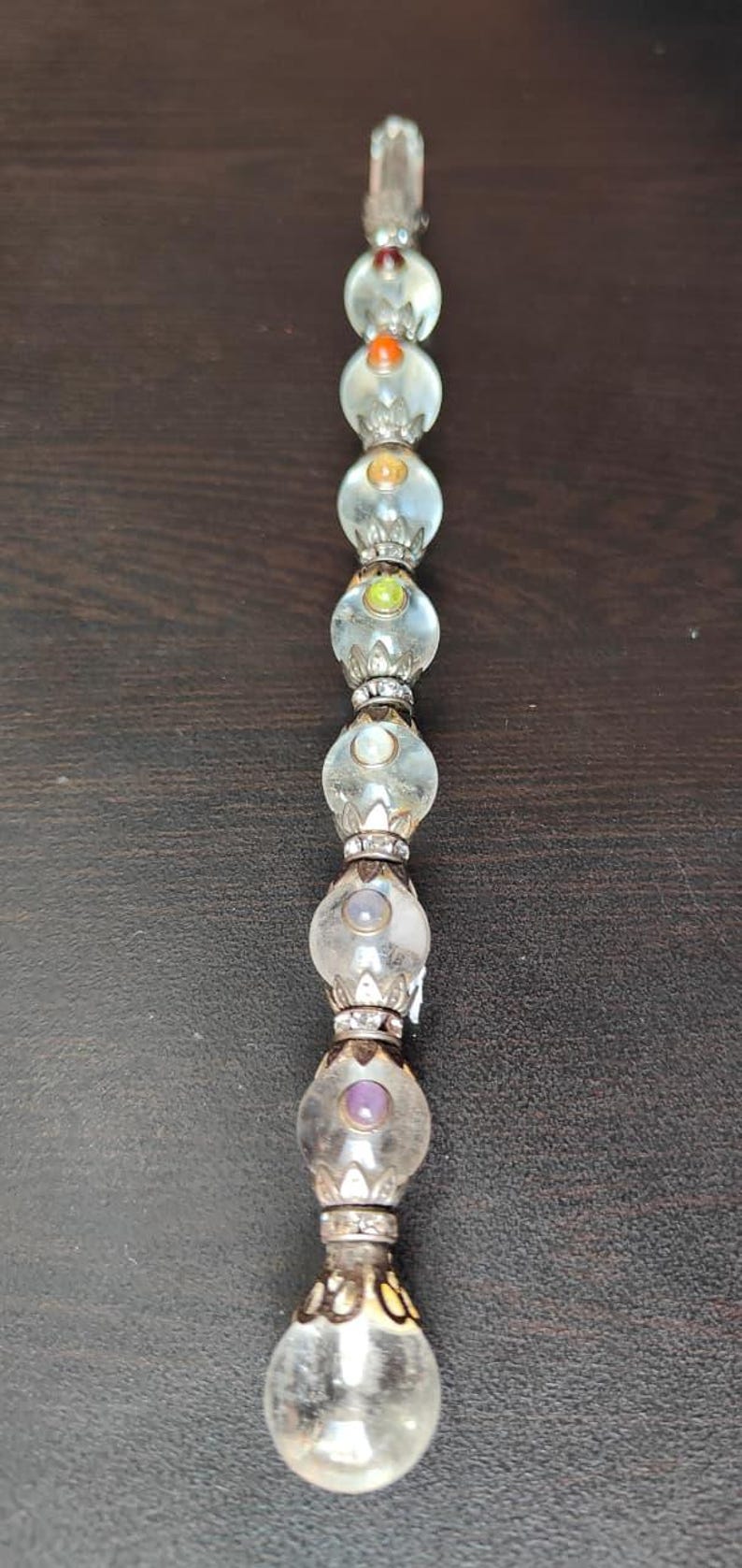 May include: A clear glass wand with a series of round, colourful beads. The beads are accented with silver-coloured metal and contain small, coloured gems. The wand is a decorative item.