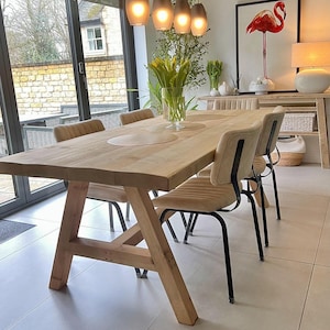 May include: A wooden dining table with a natural finish and beige upholstered chairs with black metal legs. The room includes a flamingo art print, pendant lights, and a vase of yellow tulips. The word "WAX" is printed at the bottom.