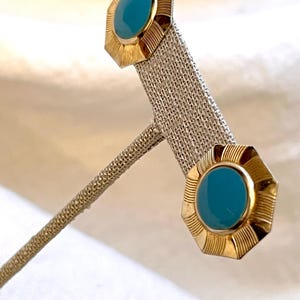 Könnte beinhalten: Ein Paar goldfarbene Ohrringe mit türkisblauen Cabochonsteinen, die in einer geometrischen Form gefasst sind.