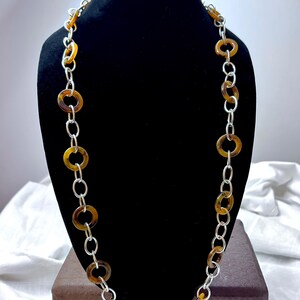 May include: A long necklace with a silver chain and brown tortoise shell-like round beads.