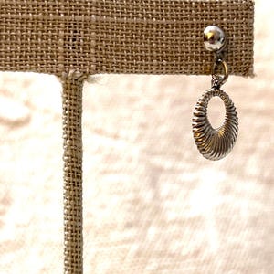 Peut inclure: Boucles d'oreilles créoles argentées avec un design texturé. Les boucles d'oreilles sont sur un présentoir.