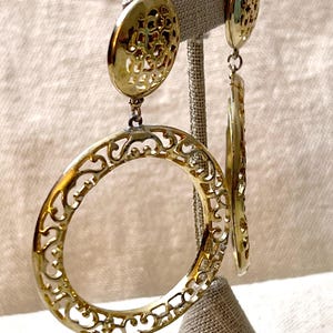 May include: Gold filigree earrings with a large circular design and a smaller circular design at the top.
