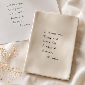 Puede incluir: Un plato rectangular de cerámica en color blanco roto con el texto impreso en negro: I choose you. Today and every day. Always & forever. ♡ -mason. El plato está colocado junto a una tarjeta a juego con el mismo texto y una rama de flores secas.