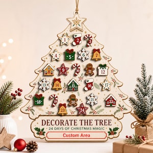 May include: A wooden Christmas tree-shaped advent calendar featuring 24 numbered icons including stars, stockings, candy canes, bells, gifts, and gingerbread men. The base displays the text DECORATE THE TREE 24 DAYS OF CHRISTMAS MAGIC.