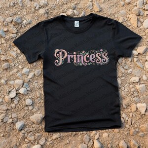 Pode incluir: Camiseta preta com a palavra "Princess" em uma fonte decorativa multicolorida. O texto é adornado com desenhos florais e redemoinhos. A camiseta é feita de um material macio e é adequada para uso casual.