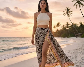May include: A cream-colored halter top and a patterned wrap skirt with a high slit. The skirt features a black and tan design with a yellow and pink border. The outfit is worn on a sandy beach with palm trees.