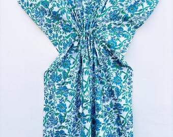 May include: A white caftan with a blue and green floral pattern, hanging on a black hanger. The caftan has a V-neck and a gathered waist. The floral design includes detailed flowers and leaves.