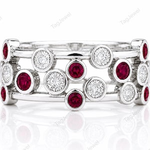 May include: A silver-toned ring featuring a multi-band design with bezel-set circular stones. The ring is decorated with alternating round red rubies and clear white diamonds arranged in a scattered, bubble-like pattern across the metal bands.
