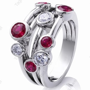 May include: A multi-band silver ring featuring a series of bezel-set round rubies and clear white diamonds. The design consists of three interconnected bands that hold the alternating red and clear stones in a staggered, layered arrangement.