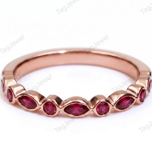 Könnte beinhalten: Ein Ring aus Roségold mit einem abwechselnden Muster aus runden und marquiseförmigen roten Rubinen in Zargenfassung. Der Ring hat eine polierte metallische Oberfläche und ein durchgehendes Design, das den gesamten Ring umfasst.