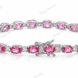 Puede incluir: Una pulsera de tenis en tono plateado que presenta una serie de piedras preciosas rosas de corte ovalado alternadas con pequeñas piedras redondas transparentes. La pulsera incluye un cierre de caja metálico seguro con pestillo de seguridad.