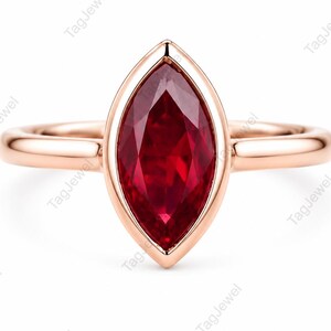 Può includere: Un anello in oro rosa con una gemma rosso intenso taglio marquise, incastonata in una montatura a lunetta liscia. La fascia è lucida e arrotondata, offrendo una cornice pulita e semplice per la forma allungata e appuntita della pietra.