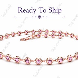 Puede incluir: Una pulsera de cadena en oro rosa que presenta una serie de piedras preciosas rosas redondas engastadas en bisel. La pulsera incluye un cierre de mosquetón y se muestra debajo del texto Ready To Ship con una línea divisoria floral decorativa.