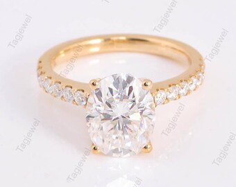 May include: A gold engagement ring with a large oval-cut diamond center stone. The band is also adorned with smaller diamonds. The ring is set against a white background, highlighting its sparkle and design.