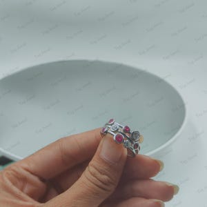 Op de afbeelding: Een zilverkleurige ring met een ontwerp van meerdere banden en rond gezette stenen. De stenen wisselen af tussen helderwitte en felroze kleuren, wat zorgt voor een gelaagd uiterlijk over het oppervlak van de metalen bandstructuur.