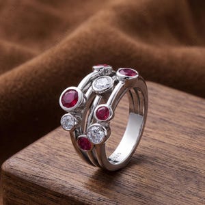 Handcrafted 925 sterling silver cluster ring featuring vibrant round lab-created ruby gemstones and sparkling white accent stones in a modern bubble-inspired bezel setting. This elegant July birthstone statement ring offers contemporary style for everyday wear, anniversaries, birthdays, engagements, Valentine's Day, Mother's Day, and thoughtful gifts for women.