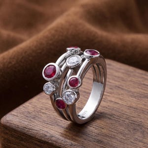 Handcrafted 925 sterling silver cluster ring featuring vibrant round lab-created ruby gemstones and sparkling white accent stones in a modern bubble-inspired bezel setting. This elegant July birthstone statement ring offers contemporary style for everyday wear, anniversaries, birthdays, engagements, Valentine's Day, Mother's Day, and thoughtful gifts for women.