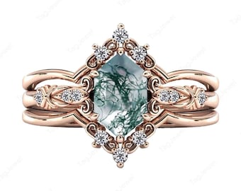 May include: A rose gold ring featuring a central hexagonal moss agate stone with green inclusions. The setting is adorned with small round white stones in a decorative frame and along the band, which has a split shank design and intricate metalwork.