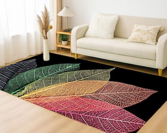May include: A rectangular area rug with a black background features a design of colorful, stylized leaves. The leaves transition from dark blue to green, yellow, orange, and red. The rug is placed in front of a white sofa.